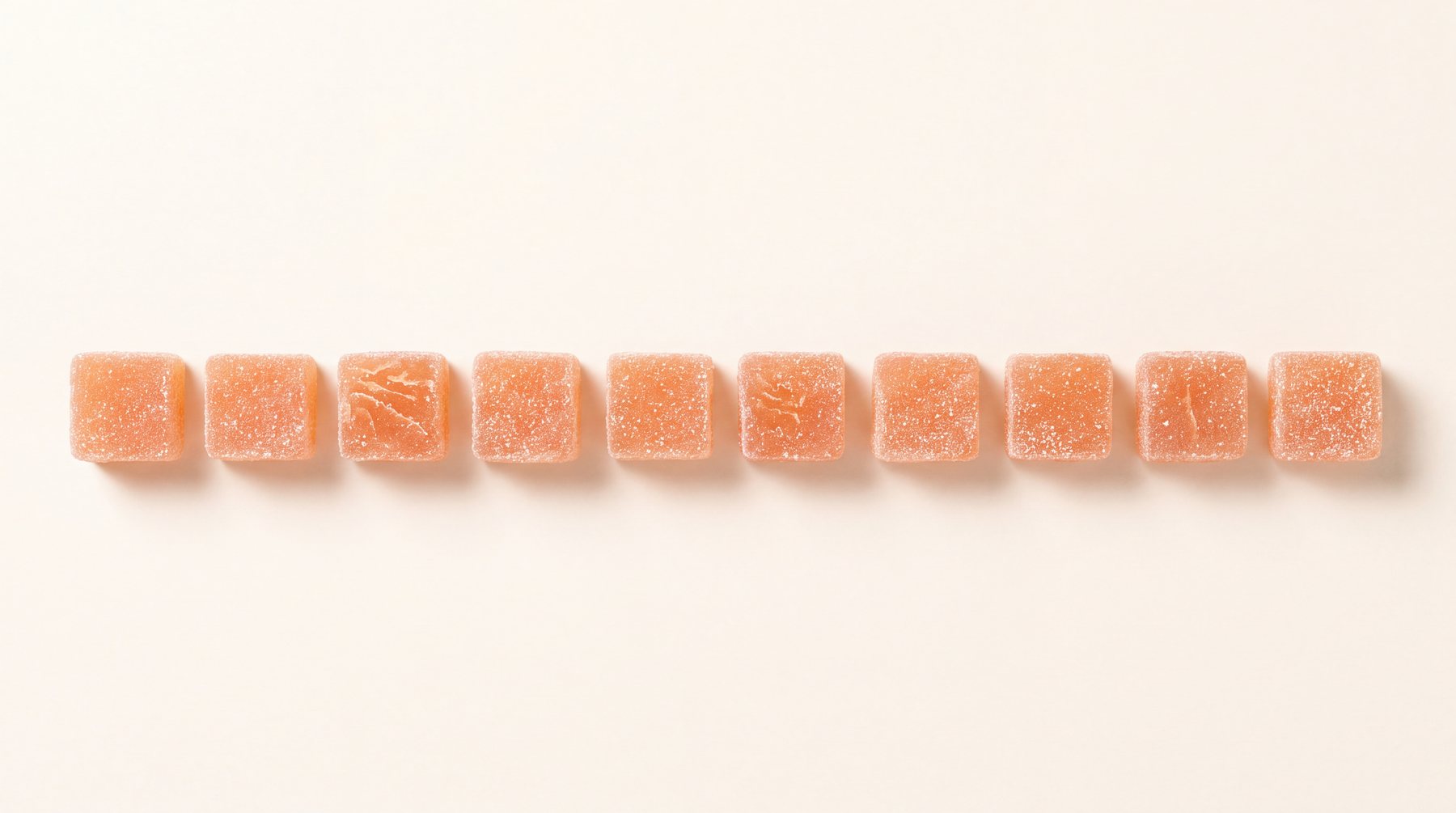 Ten sugared peach gummies in a row on cream