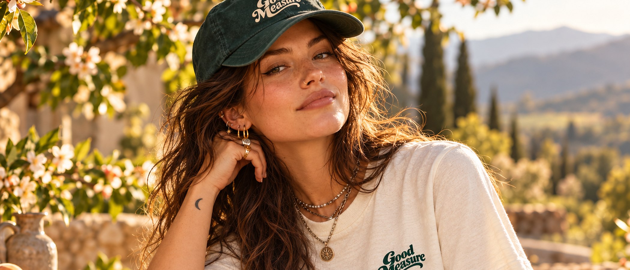 A woman in a cream Good Measure tee and pine cap in a peach orchard at golden hour