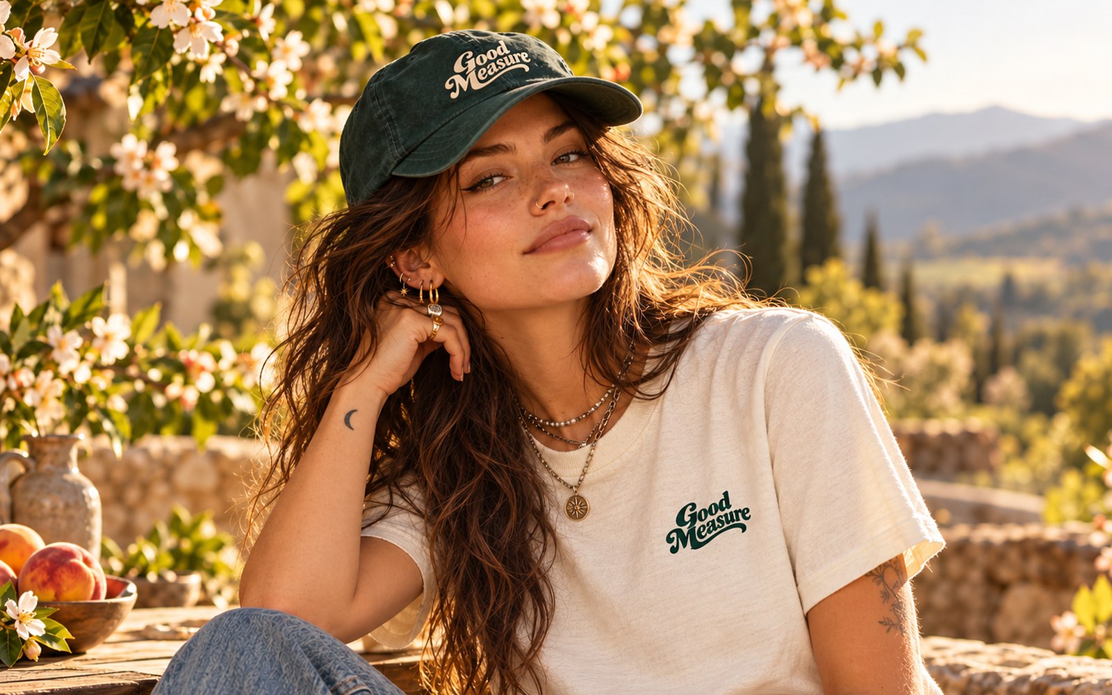 A woman in a cream Good Measure tee and pine cap in a peach orchard at golden hour
