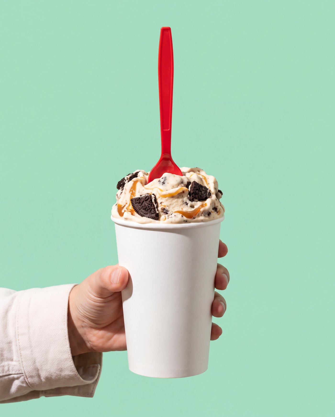 A white paper cup of thick frozen custard with cookie and caramel, held upside down