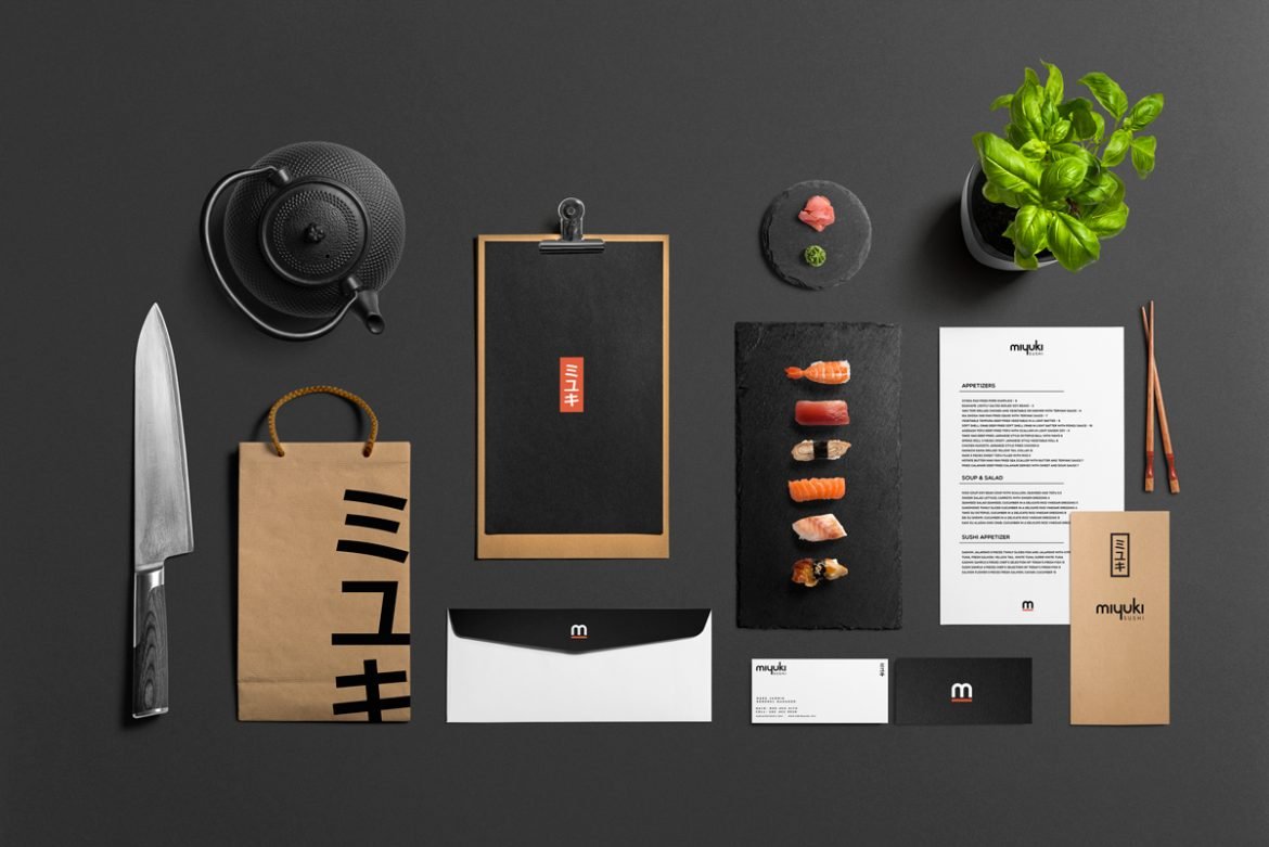 A kraft paper Miyuki takeaway bag, a menu card and a slate of nigiri on a dark table