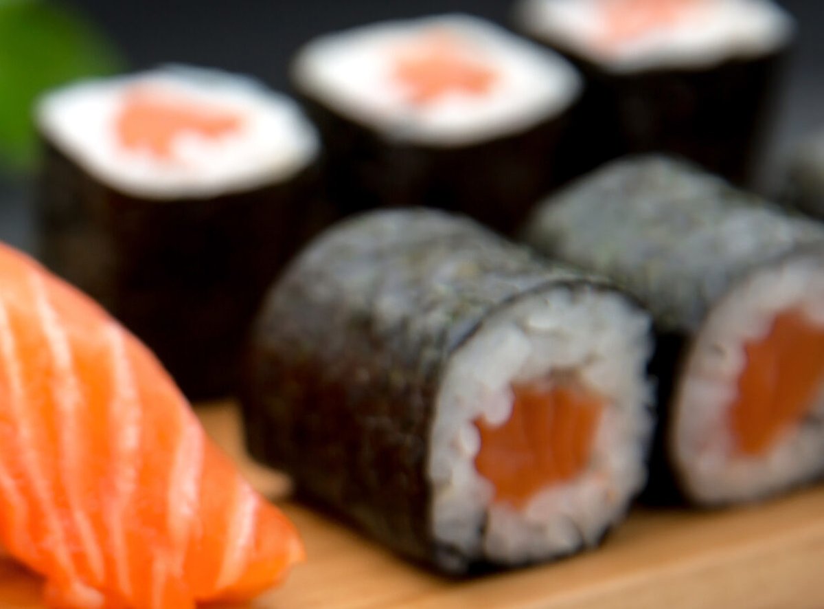 Salmon hosomaki rolls standing on a wooden board, a slice of salmon nigiri in the foreground