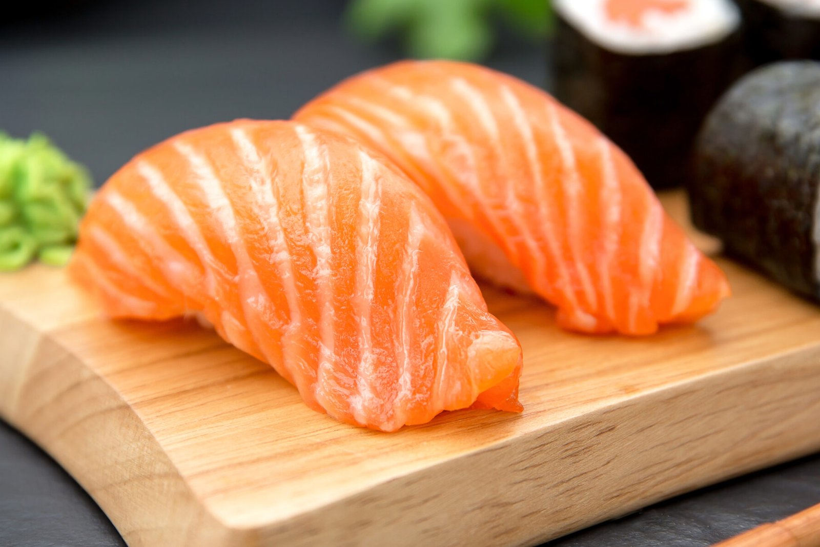 Two pieces of salmon nigiri on a pale wooden board