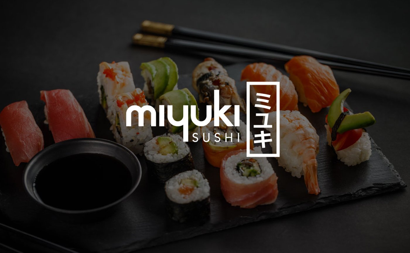 Nigiri and rolls laid out on black slate beside a dish of soy sauce and chopsticks, the Miyuki Sushi wordmark over it
