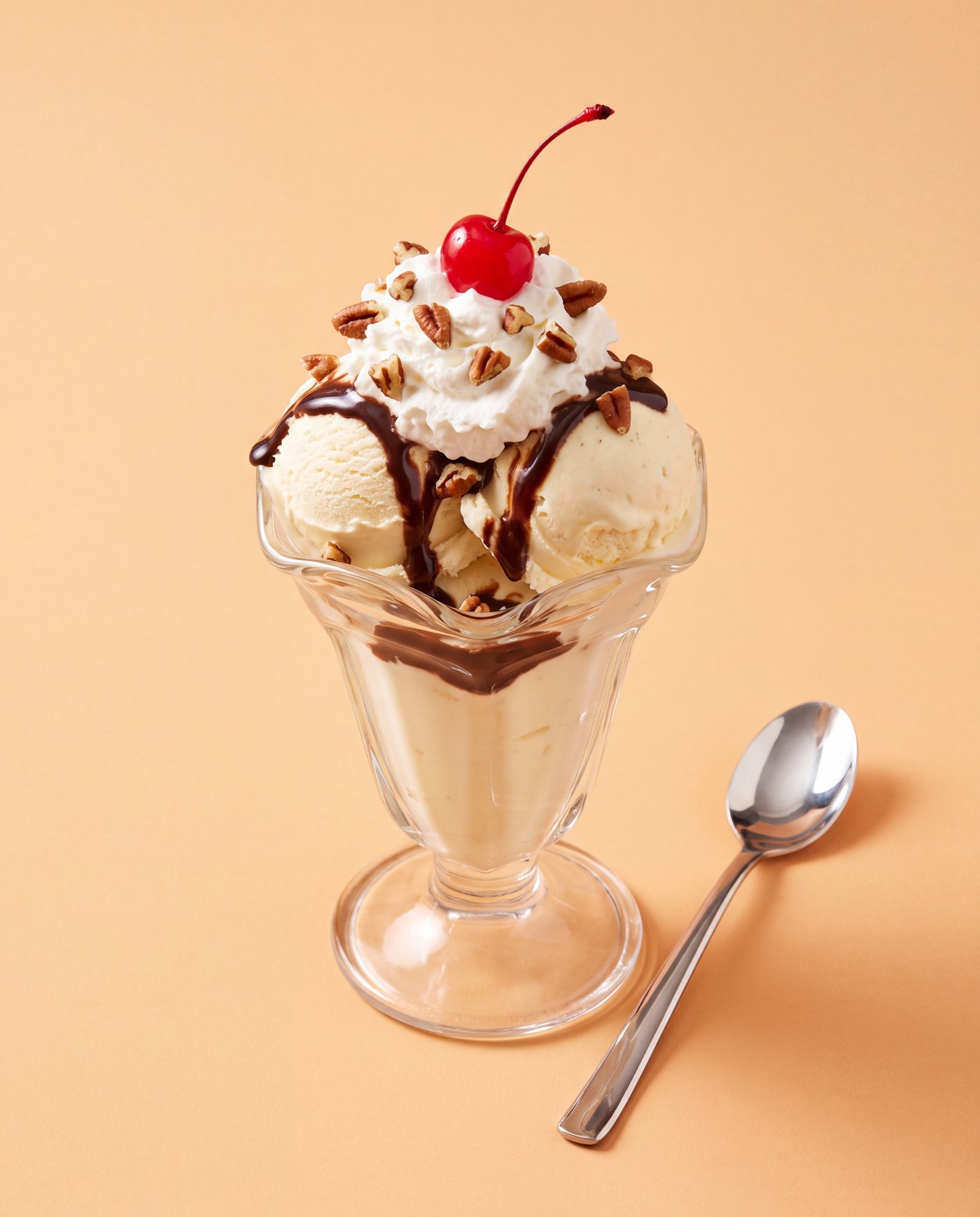 A glass tulip sundae with hot fudge, whipped cream, pecans and a cherry