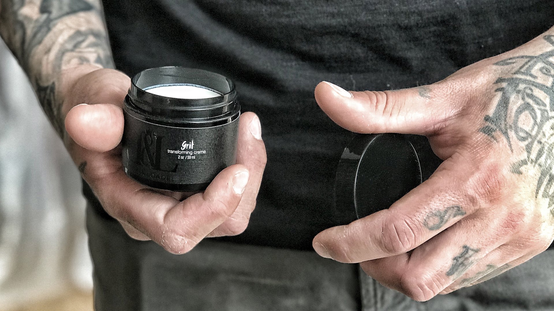 Tattooed hands opening a jar of Grit