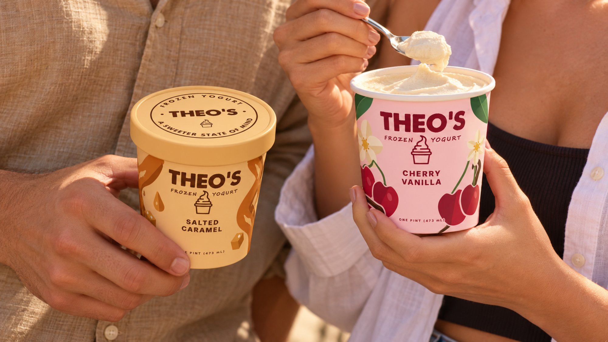 Two people in linen side by side, one holding a Theo’s Salted Caramel pint, the other spooning from a Cherry Vanilla pint