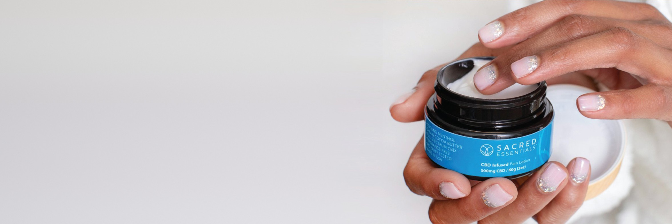 Hands holding an open jar of the Sacred Essentials Pain Lotion