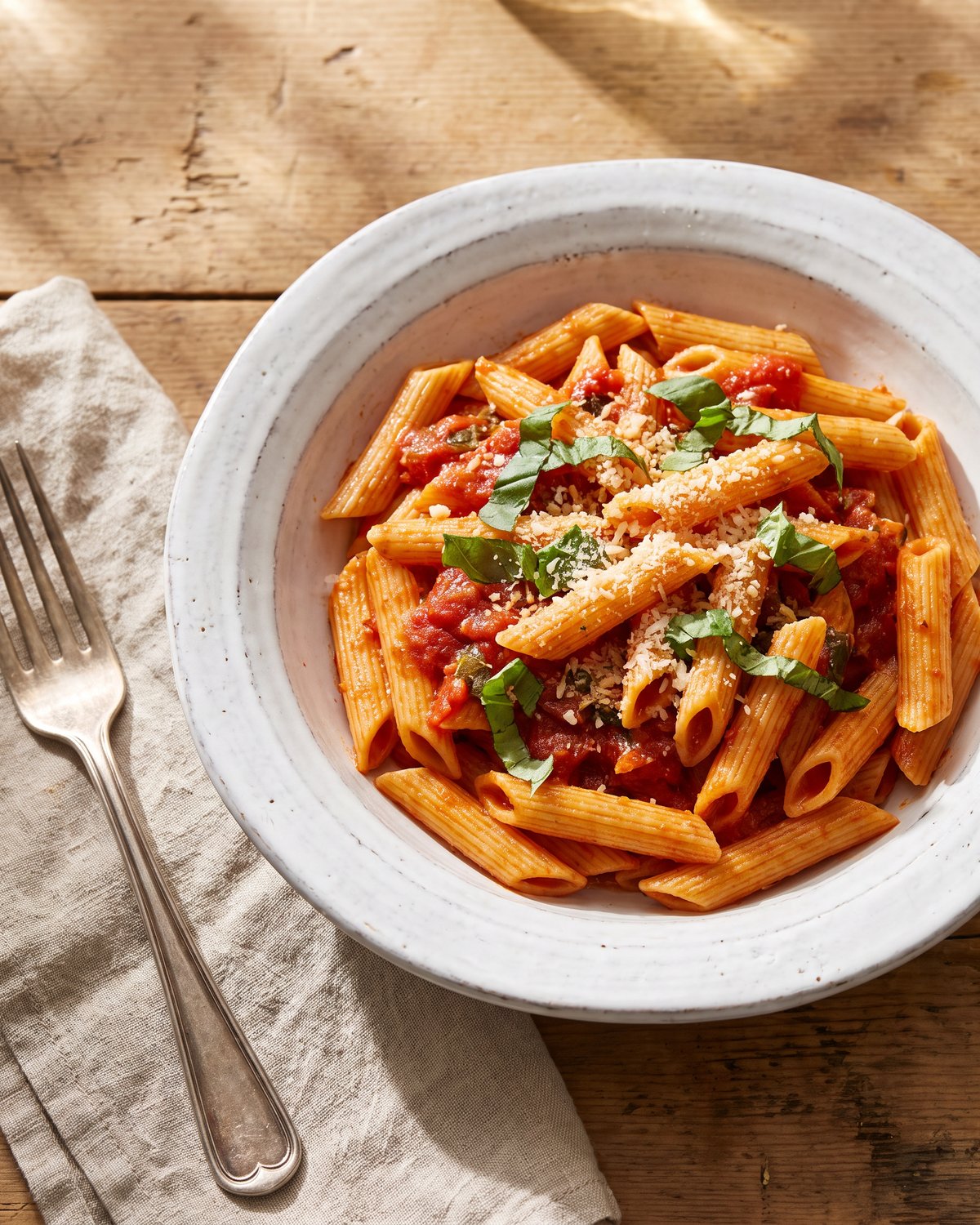 A bowl of penne in tomato basil sauce with torn basil and parmesan